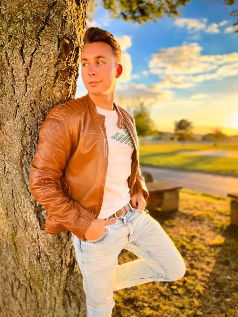 Peter Krück in a brown leather jacket leaning against a tree in the evening sun