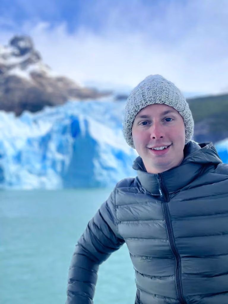 Peter Krück in a grey puffer jacket and a wool hat in front of a glacier in Patagonia